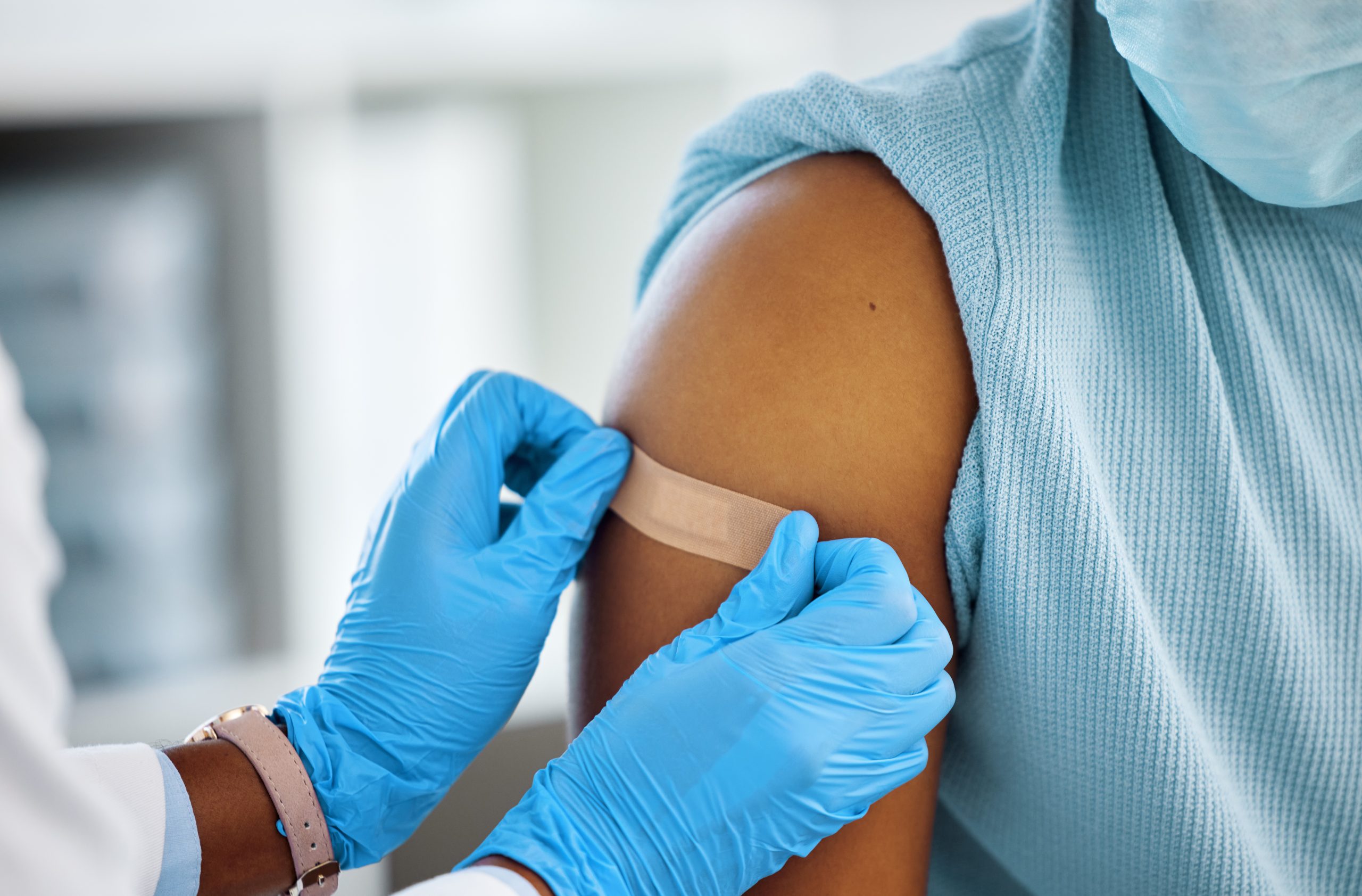 gloved hands putting a bandaid on an arm