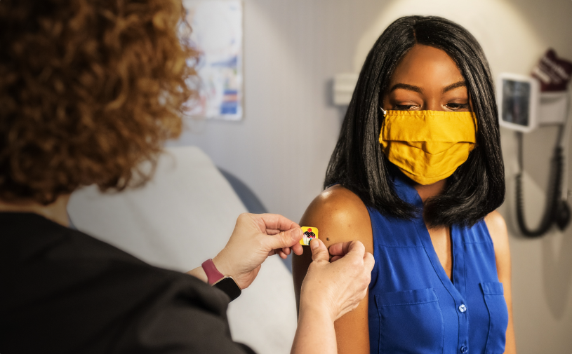 a woman putting a bandaid on a woman's arm
